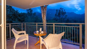 Ein Balkon mit zwei Korbstühlen und einem kleinen runden Tisch, auf dem eine Kaffeekanne und eine Tasse stehen.