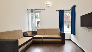 Ein Wohnzimmer mit einem Ecksofa, einem flachbildfernseher an der Wand und einem Fenster mit Vorhängen.