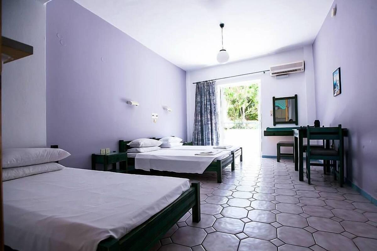 Habitación de hotel con dos camas, un escritorio, una silla y una ventana con cortinas.