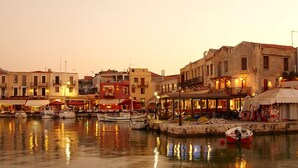 A waterfront area with buildings, boats, and outdoor seating areas. - Julia Apartments (Rethymno)