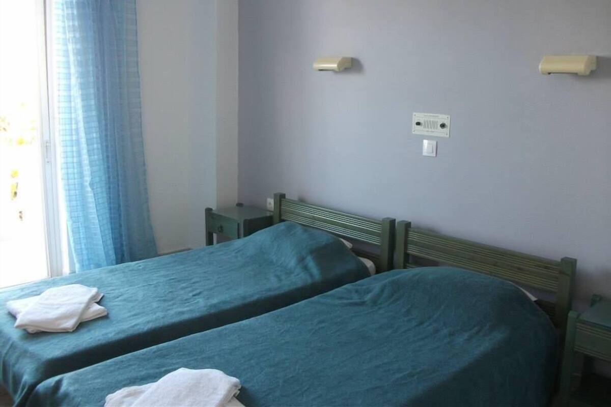 Una habitación con dos camas, una ventana con cortinas azules e interruptor de luz en la pared.