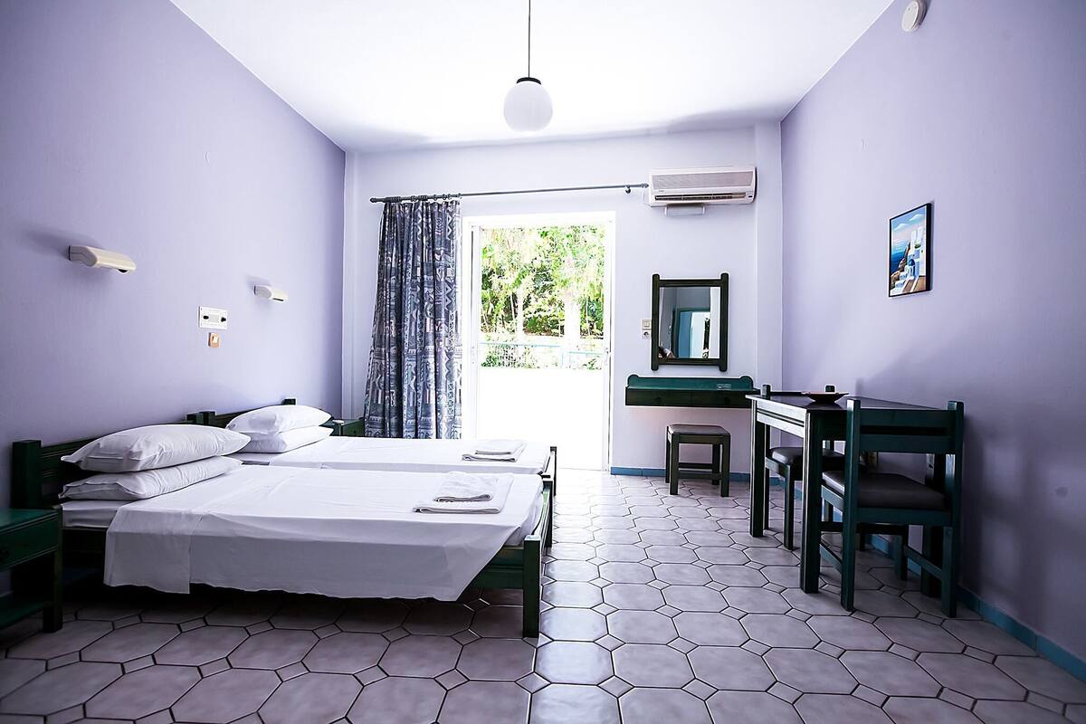 Habitación con dos camas, un escritorio, una silla y una ventana con cortinas.