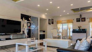 A modern living room with a white sofa, a black leather couch, and a white coffee table. There is a kitchen area with a black countertop and white cabinets.