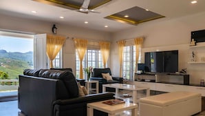 A modern living room with a black leather sofa, a white ottoman, and a flat-screen TV.