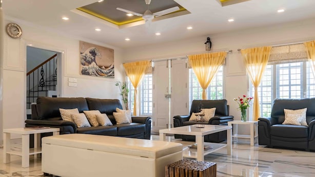 A modern living room with a black leather sofa set, white coffee tables, and a large white ottoman.