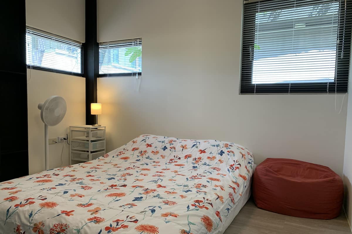 Un dormitorio con cama, mesita de noche, lámpara, ventilador y ventana con persianas.