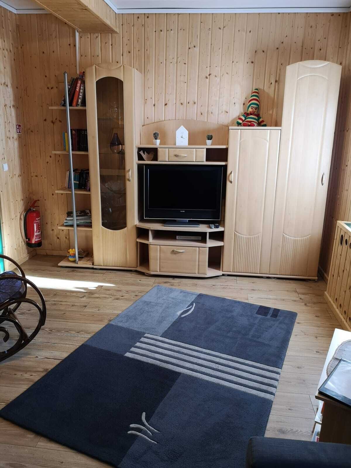 Ein gemütlicher Raum mit Holzvertäfelung, einem Flachbildfernseher auf einem Holzbodenständer, einem Bücherregal und einem Feuerlöscher.