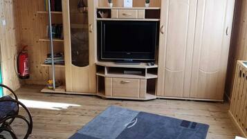 Ein gemütlicher Raum mit Holzvertäfelung, einem Flachbildfernseher auf einem Holzbodenständer, einem Bücherregal und einem Feuerlöscher.