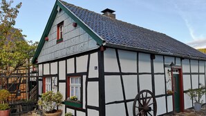 A traditional half-timbered house with a steeply pitched roof, a large wooden wheel, and a small garden area with potted plants. - Ferienhof Schmickerath (Simmerath)