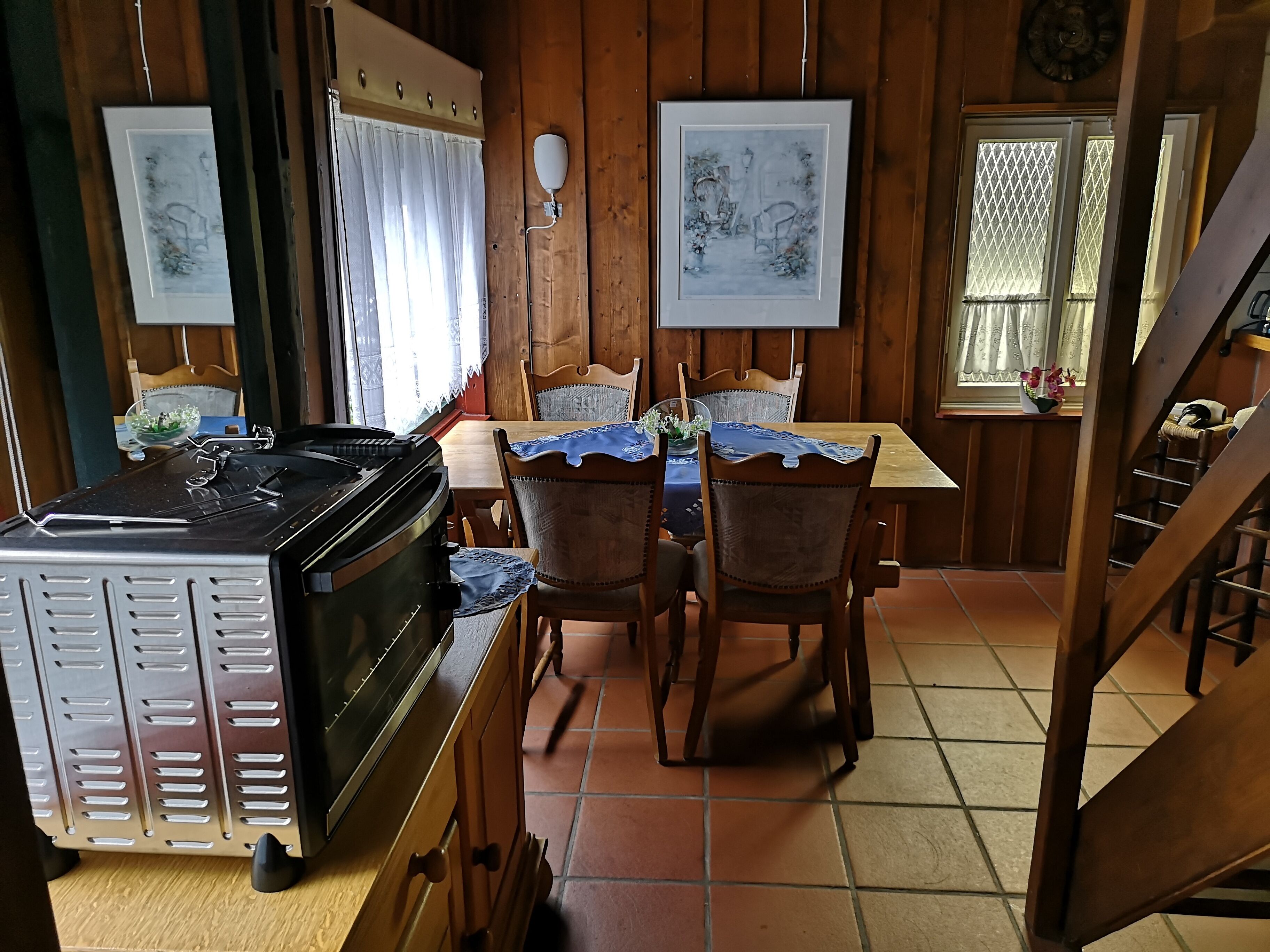 Une pièce aux murs lambrissés, comprenant une table à manger, des chaises, un poêle et des œuvres d’art encadrées.