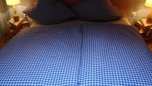 Un letto rifatto con cura, coperto da una tenda a quadri blu e bianca, con due cuscini abbinati e due lampade ai comodini in legno.
