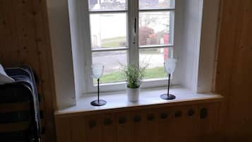 A room with a wooden floor, a window with a white frame, and a small potted plant on the windowsill.