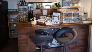 Un bancone di pasticceria con dolci e una macchina per caffè. Si vedono scaffali con articoli in vetro e una lavagna con il menu.