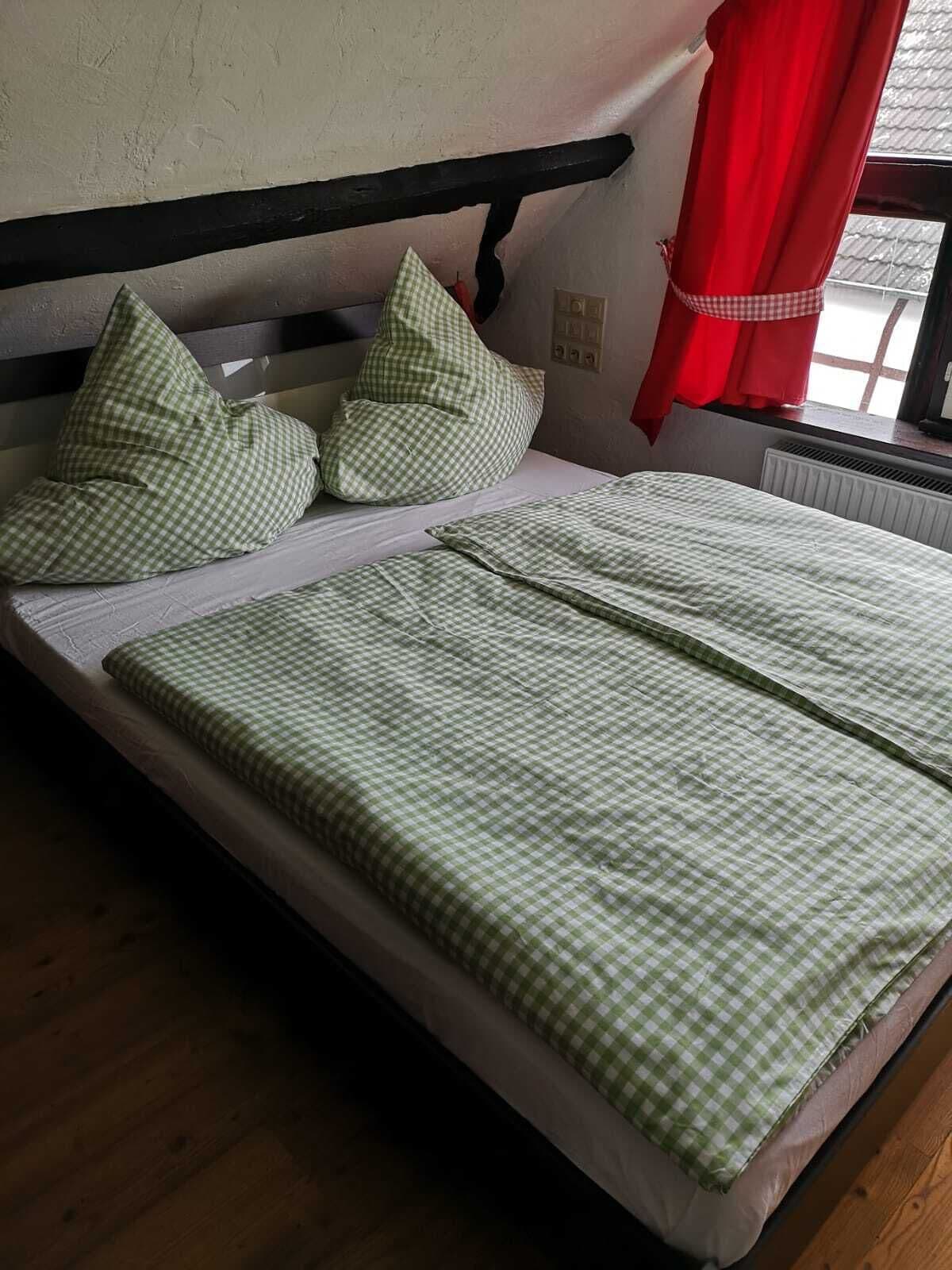 Una cama con ropa de cama y almohadas a cuadros verdes, cabecera negra y cortina roja.