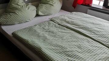 Una cama con ropa de cama y almohadas a cuadros verdes, cabecera negra y cortina roja.
