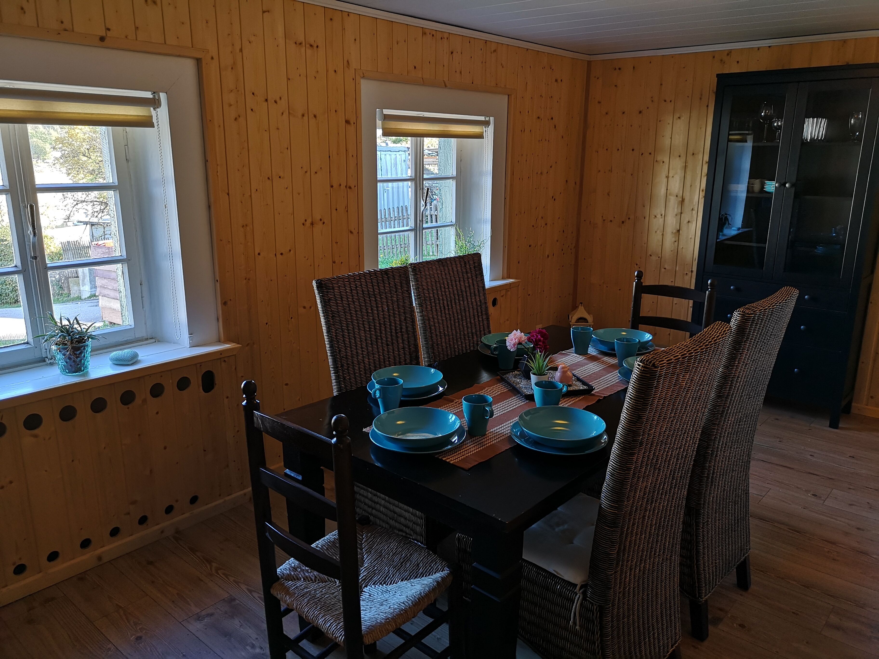 A dining area with a wooden interior, a black table set with blue plates and cups, and wicker chairs.