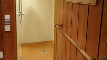 A wooden door with a metal handle, a tiled shower area, and a wall-mounted light fixture.