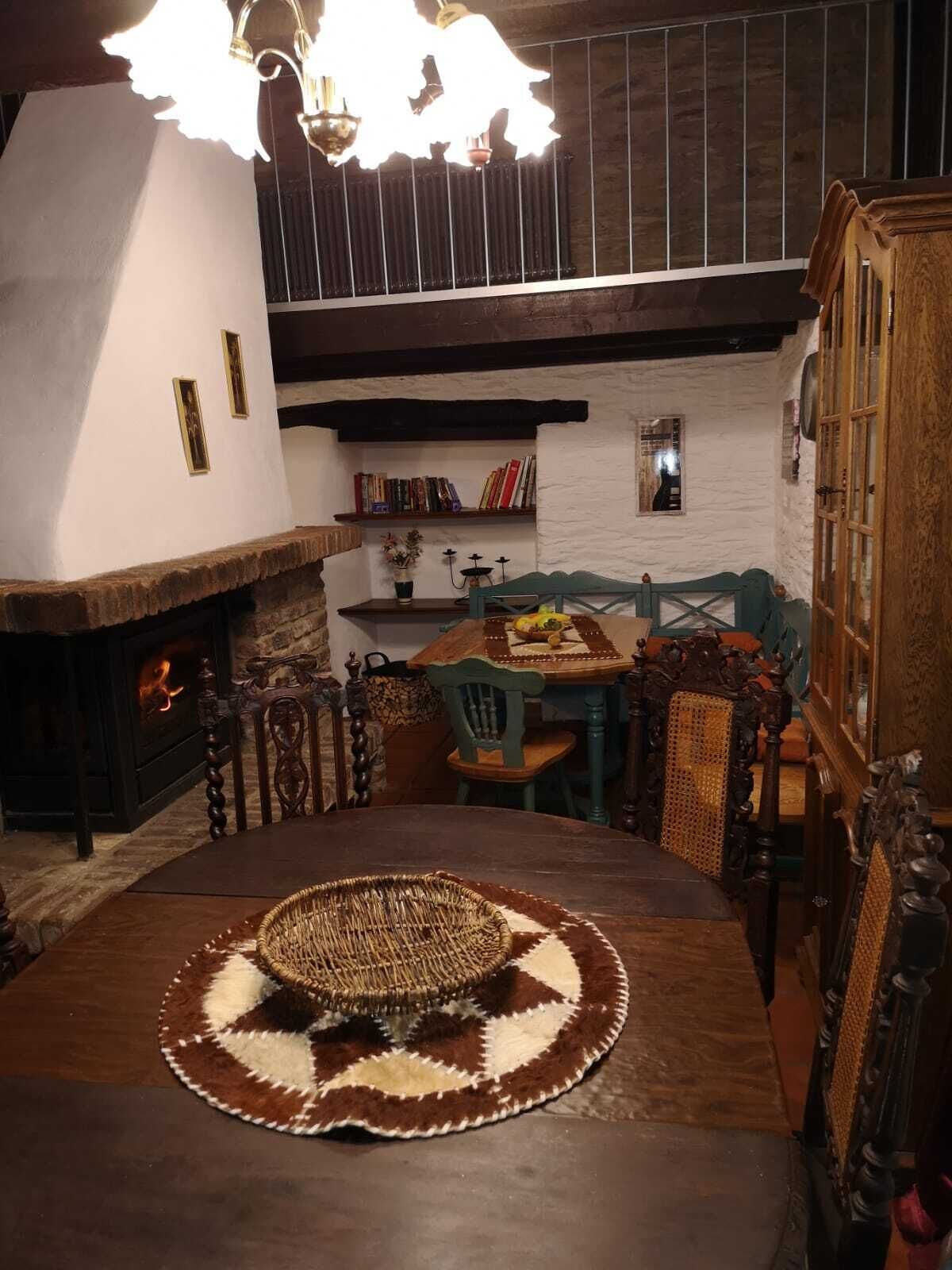 A cozy room with a fireplace, a dining table with a patterned runner, and a bookshelf filled with books.