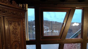 A room with a wooden cabinet with intricate carvings, a white sofa with patterned cushions, and large windows offering a view of a snowy landscape. - Ferienhof Schmickerath (Simmerath)