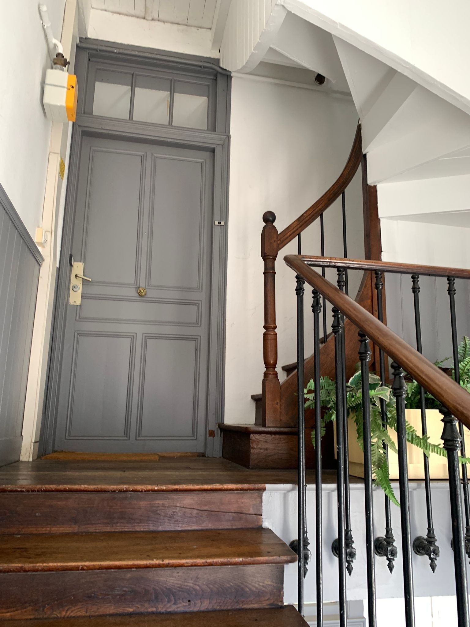 A staircase with wooden steps and a black metal railing, leading to a grey door with a brass doorknob.