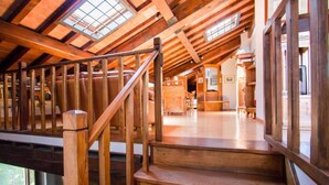 Una escalera de madera conduce a una zona elevada con tragaluces, vigas de madera y vistas al interior.