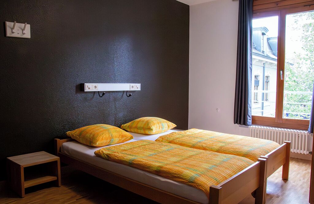 Ein Schlafzimmer mit Bett, Nachttisch, Steckdose und Fenster.