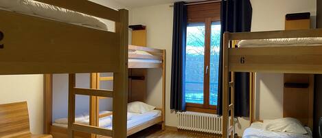A room with bunk beds, a wooden chair, a radiator, and a window with curtains.