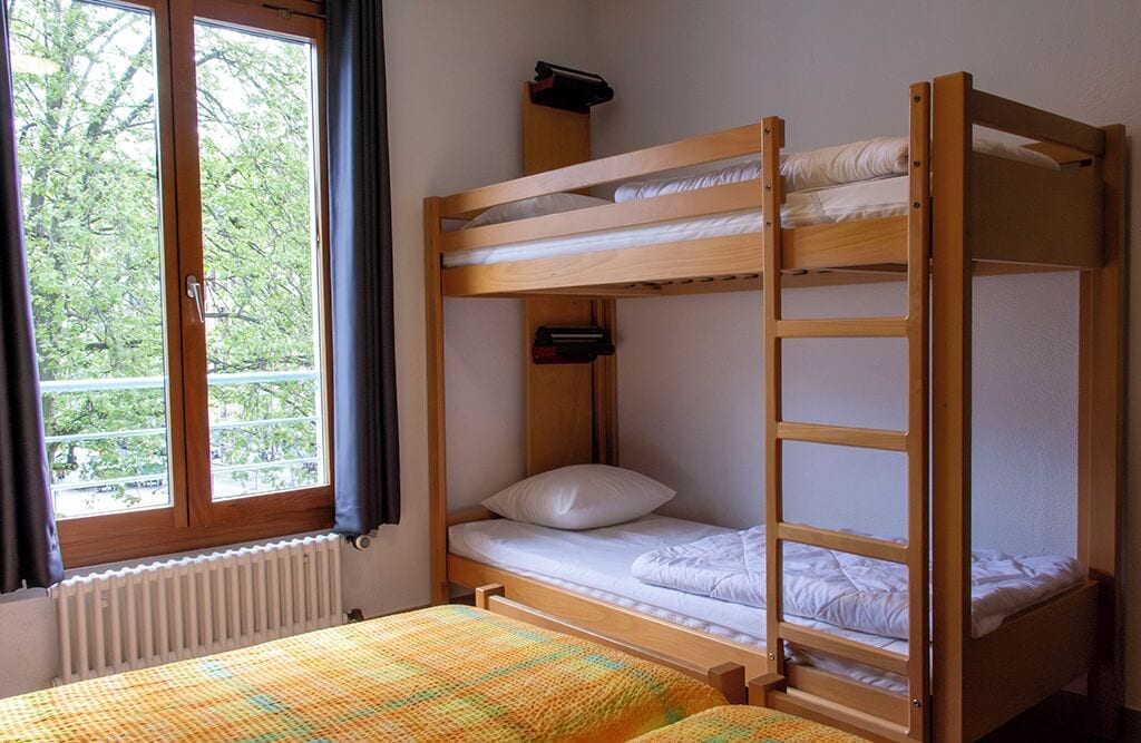 A bunk bed room with a window, a radiator, and a bed with a colorful blanket.