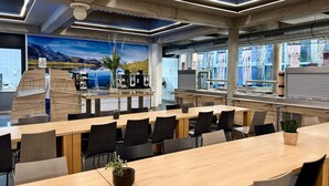 Una sala de conferencias moderna con una larga mesa, sillas, una estación de café y un mural de un paisaje montañoso.