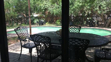 Un patio al aire libre con una mesa redonda y sillas, una piscina y follaje circundante.