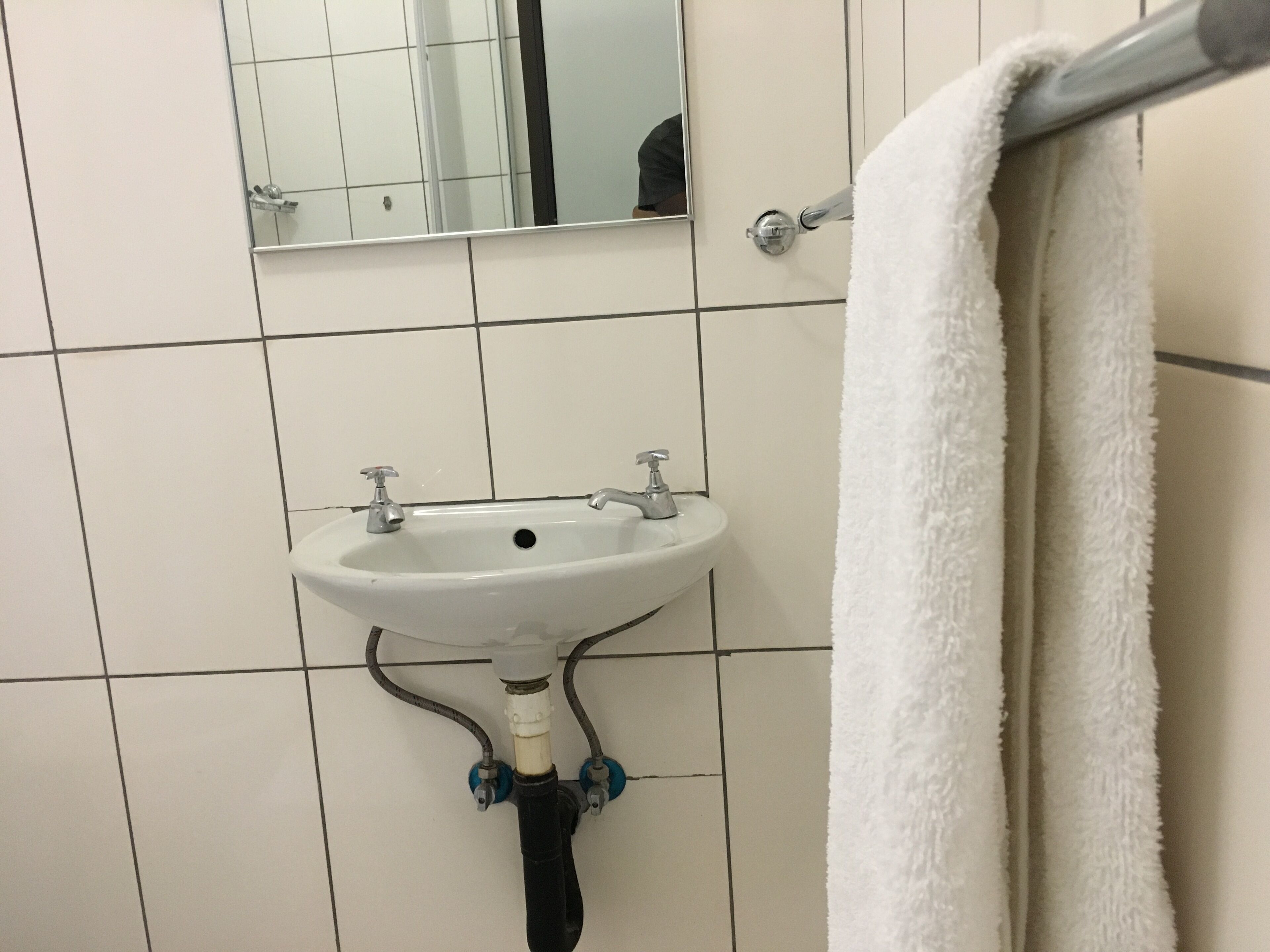 Un baño con un lavamanos blanco, un espejo encima y una toalla colgada en un perchero.