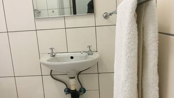 Un baño con un lavamanos blanco, un espejo encima y una toalla colgada en un perchero.
