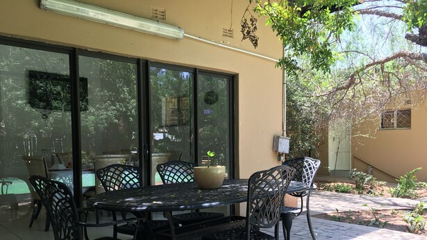 An outdoor patio with a table and chairs, a potted plant, and a view of the surrounding greenery. - Havilla Guest House (Gaborone)