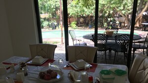 A dining area with a table set for four, including plates, cutlery, and a glass pitcher. Outside, there is a pool and outdoor seating. - Havilla Guest House (Gaborone)