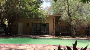 A pool area with a building adjacent to it, surrounded by trees and plants. - Havilla Guest House (Gaborone)