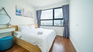 A modern bedroom with a wooden bed, a blue ottoman, a city view through a large window, and a wall-mounted desk.