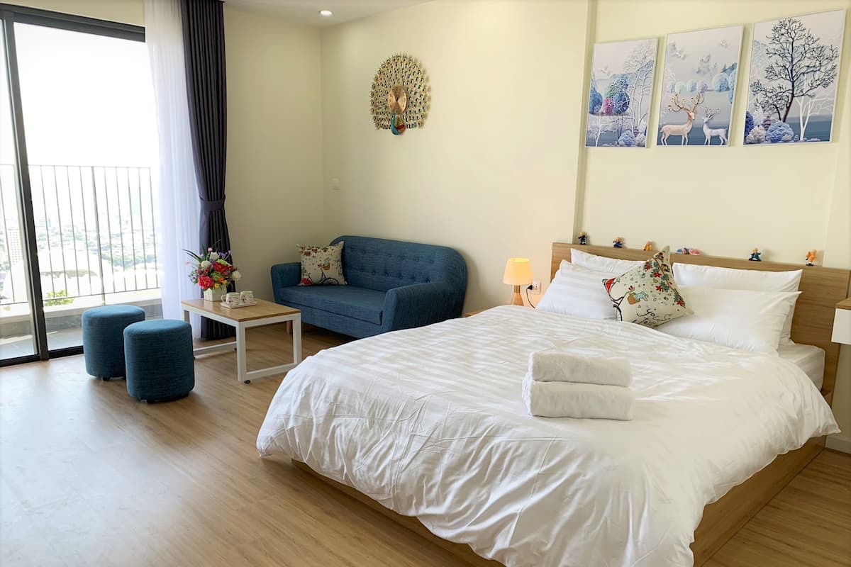A hotel room with a large bed, a blue sofa, a small table with a lamp, and a wall clock.