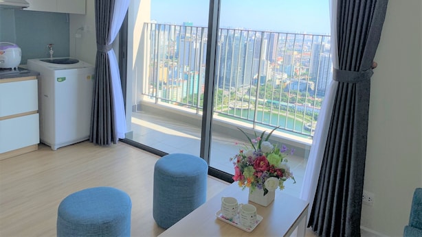 A modern apartment with a balcony, a kitchen area, and a dining space with a table and two blue ottomans.