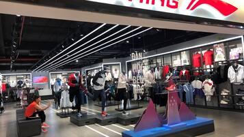 A Li-Ning store with mannequins displaying athletic wear, a prominent store sign, and a seating area with a person.