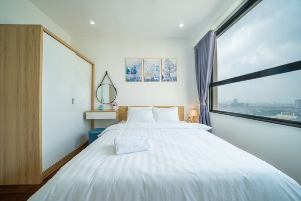 Habitación de hotel con una cama grande, una mesita de noche, un espejo y una ventana con vista a la ciudad.