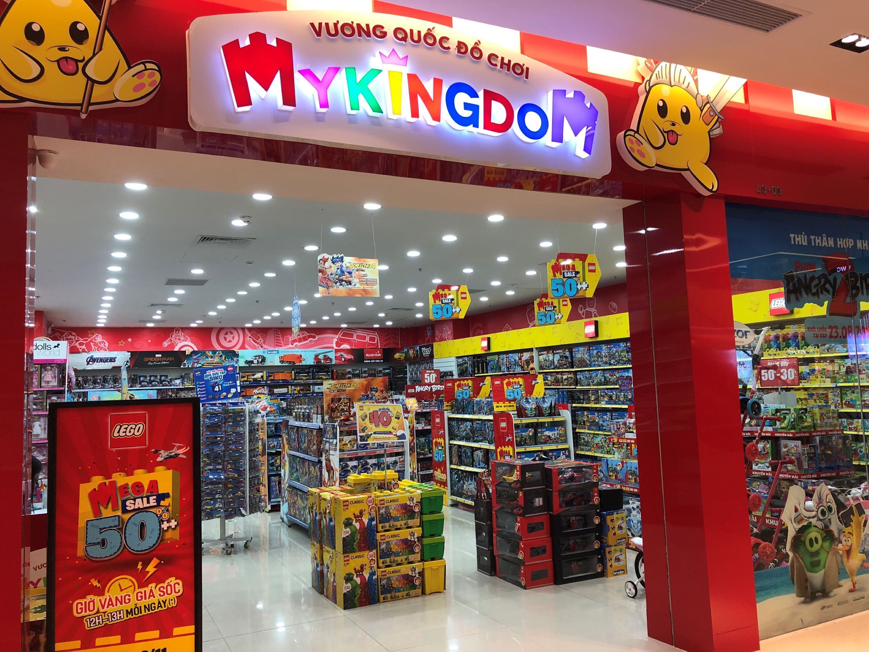 A brightly lit toy store with a prominent 'My Kingdom' sign, various toy displays, and promotional signs indicating sales.