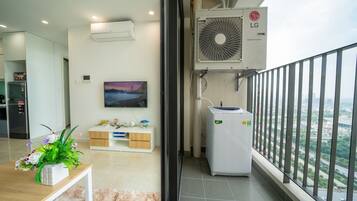 A modern apartment with a balcony, an air conditioning unit, a refrigerator, a TV, and a view of the city.