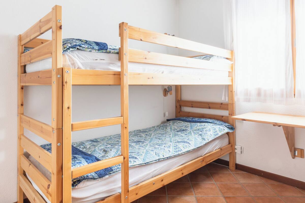 Ein Stockbett in einem Zimmer mit gefliestem Boden und einem Vorhangfenster.