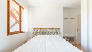 Een slaapkamer met een groot bed, een raam met houten kozijnen, een radiator en een deur.