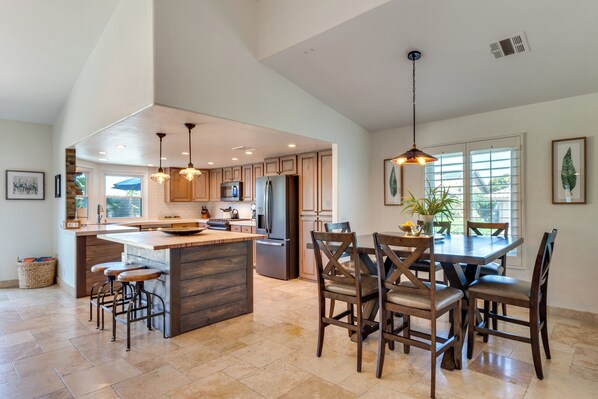 A spacious kitchen with a central island, wooden chairs, and pendant lighting.
