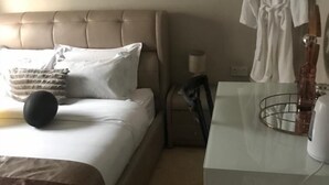Habitación de hotel con cama, mesita de noche con lámpara, bata colgada en la pared y un aspirador.