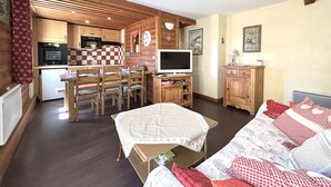 Une chambre confortable de style cabane, avec un intérieur en bois, une kitchenette, un coin repas et un lit avec une literie à carreaux.