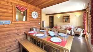 Un coin repas en bois avec une table dressée pour quatre personnes, une horloge et un panneau indiquant un café.