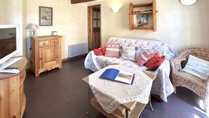 Un salon chaleureux avec un meuble en bois, un canapé agrémenté de coussins à motifs, un fauteuil en osier et une petite table sur laquelle repose un livre.