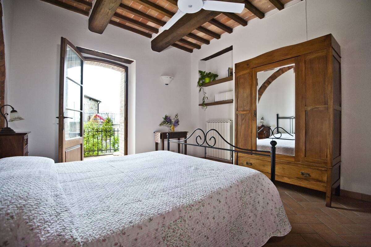 Une chambre à coucher avec un lit, une armoire en bois et une porte-fenêtre donnant sur un balcon.
